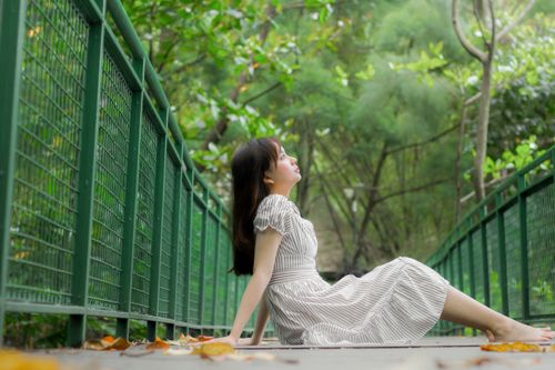 Free A young woman in a striped dress relaxes on a bridge in a lush green forest. Stock Photo