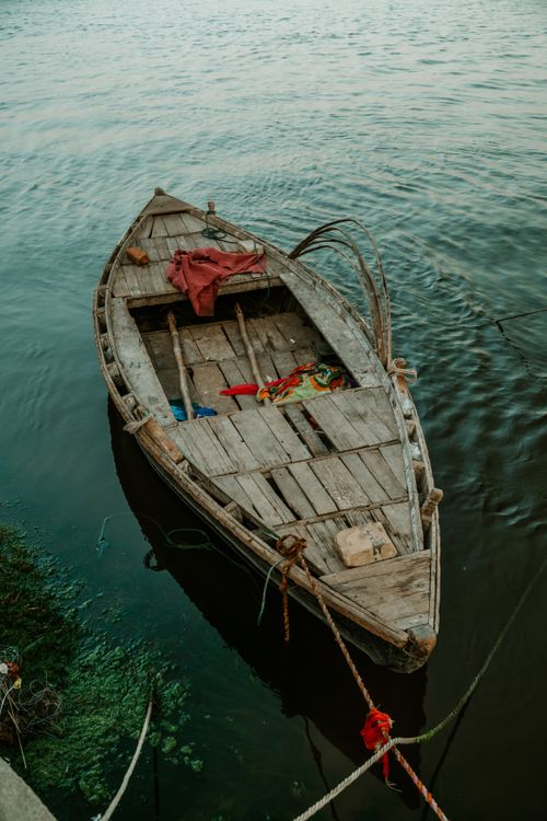 Free A rustic wooden fishing boat docked on a serene Indian river, showcasing cultural craftsmanship. Stock Photo