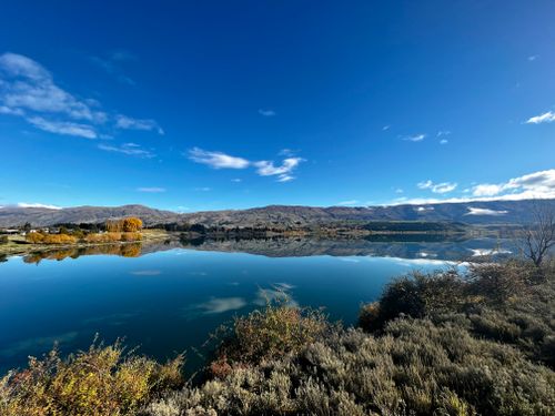 Free Beautiful panoramic view of a tranquil lake reflecting mountain ranges under a clear blue sky. Stock Photo