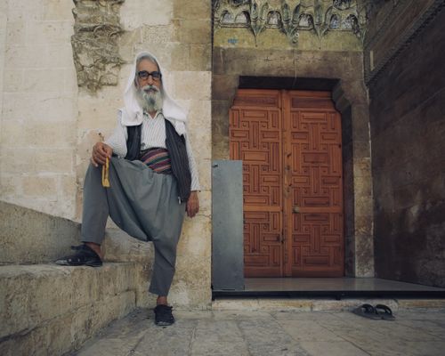 Free Elderly man with beard and eyeglasses standing by a mosque entrance, showcasing traditional attire. Stock Photo