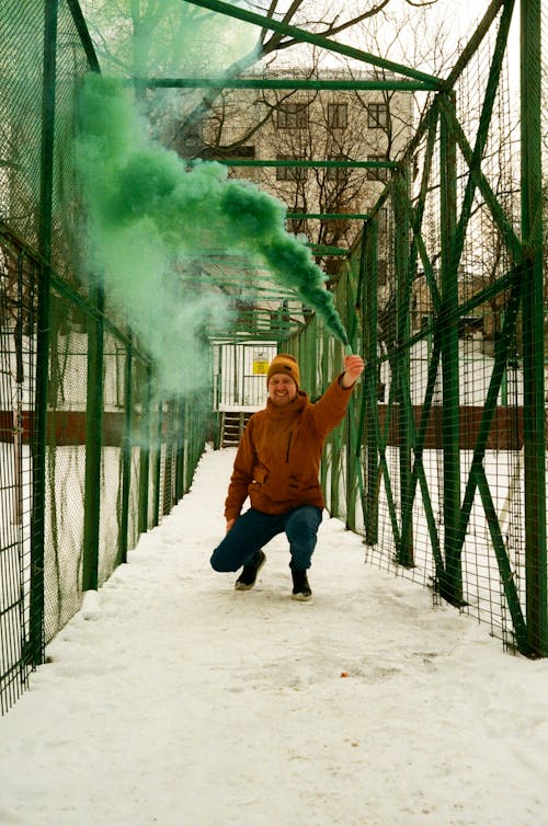 Man with a Green Smoke Flare in a Wire Fenced Walkway