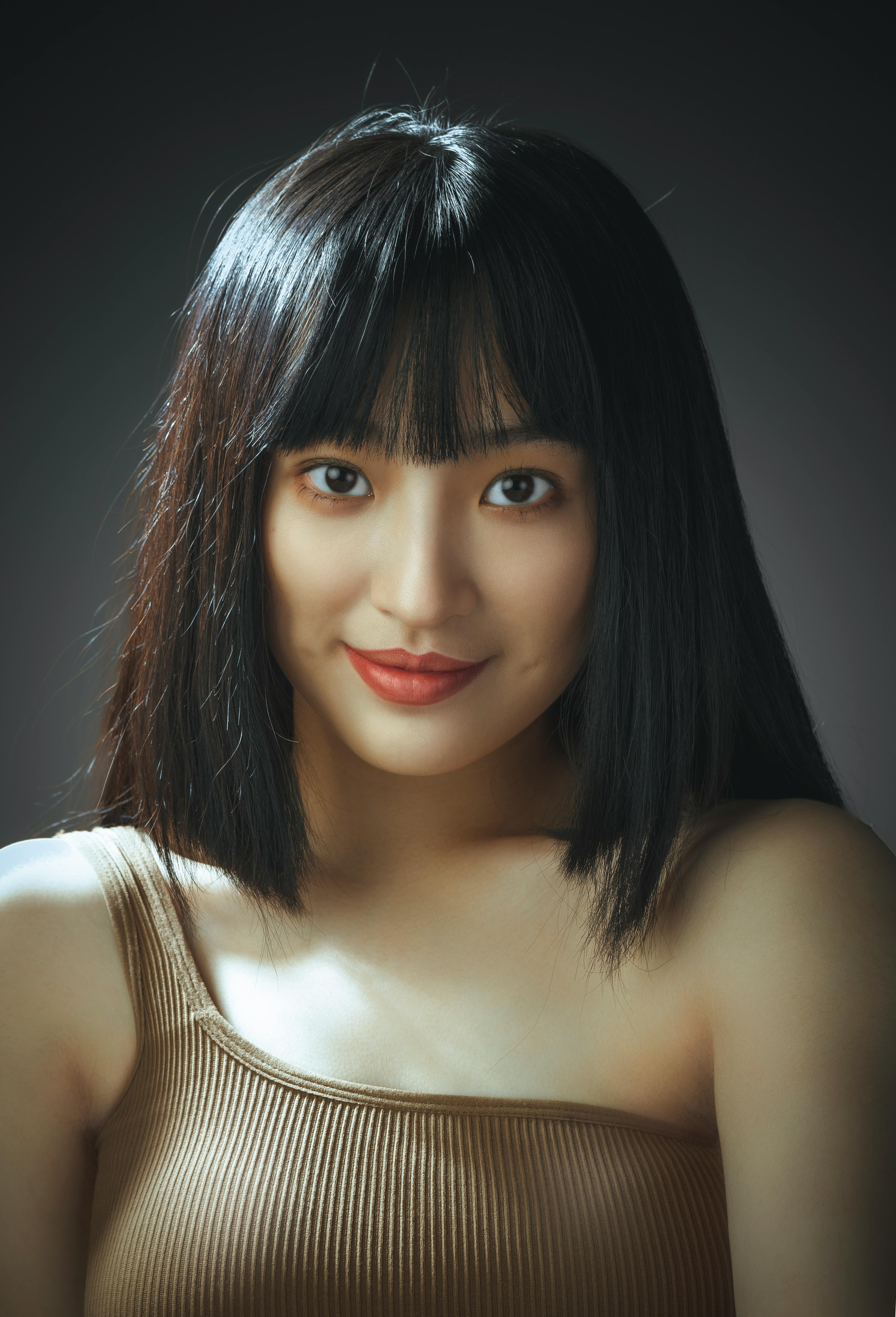 Studio portrait of a young woman with bangs, smiling softly, in a neutral background.