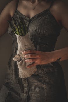 Woman in dress holds asparagus bouquet, creating a moody and artistic portrait.