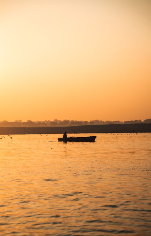 Free A tranquil scene of a lone fisherman silhouetted against a golden sunset on a calm lake. Stock Photo