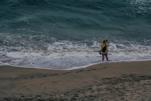 High Angle View of a Woman Standing Ankles Deep in the Sea and Taking a Picture 