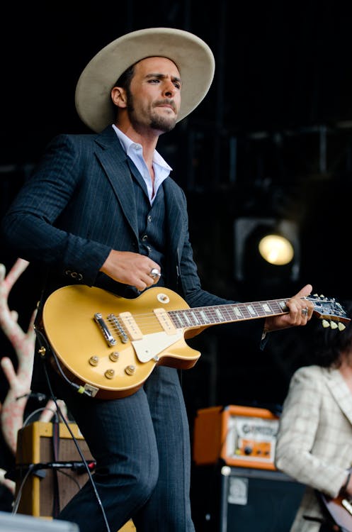 免費 黑色和白色細條紋正式外套和褲子的男人穿著米色帽子拿著棕色的電吉他 圖庫相片
