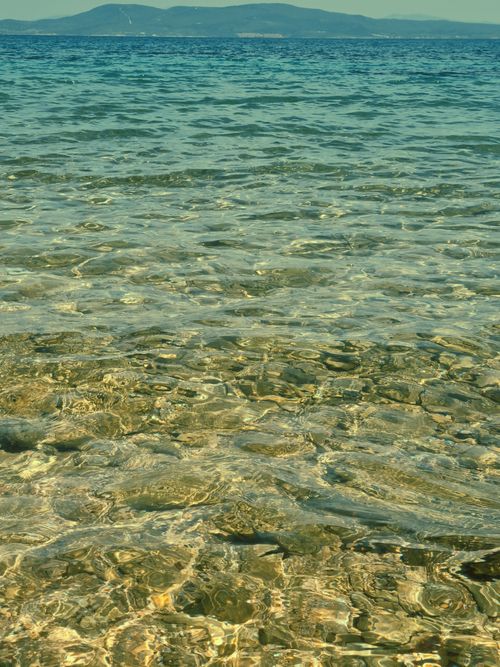 Free Transparent sea water with distant hills, perfect for a serene tropical vibe. Stock Photo