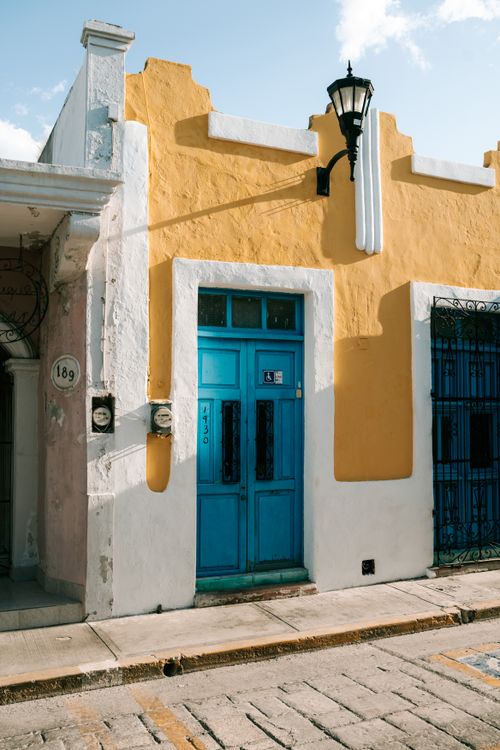 Free Vibrant urban scene showcasing a blue door on a yellow wall in a sunny street. Stock Photo