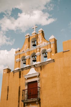 Rustic church facade with bells and balcony against a cloudy sky in Mexico.