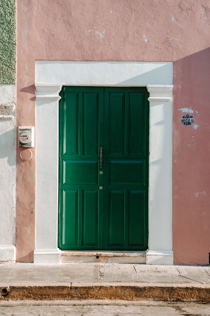 A vibrant green door on a colorful Mexican townhouse facade captures urban charm.