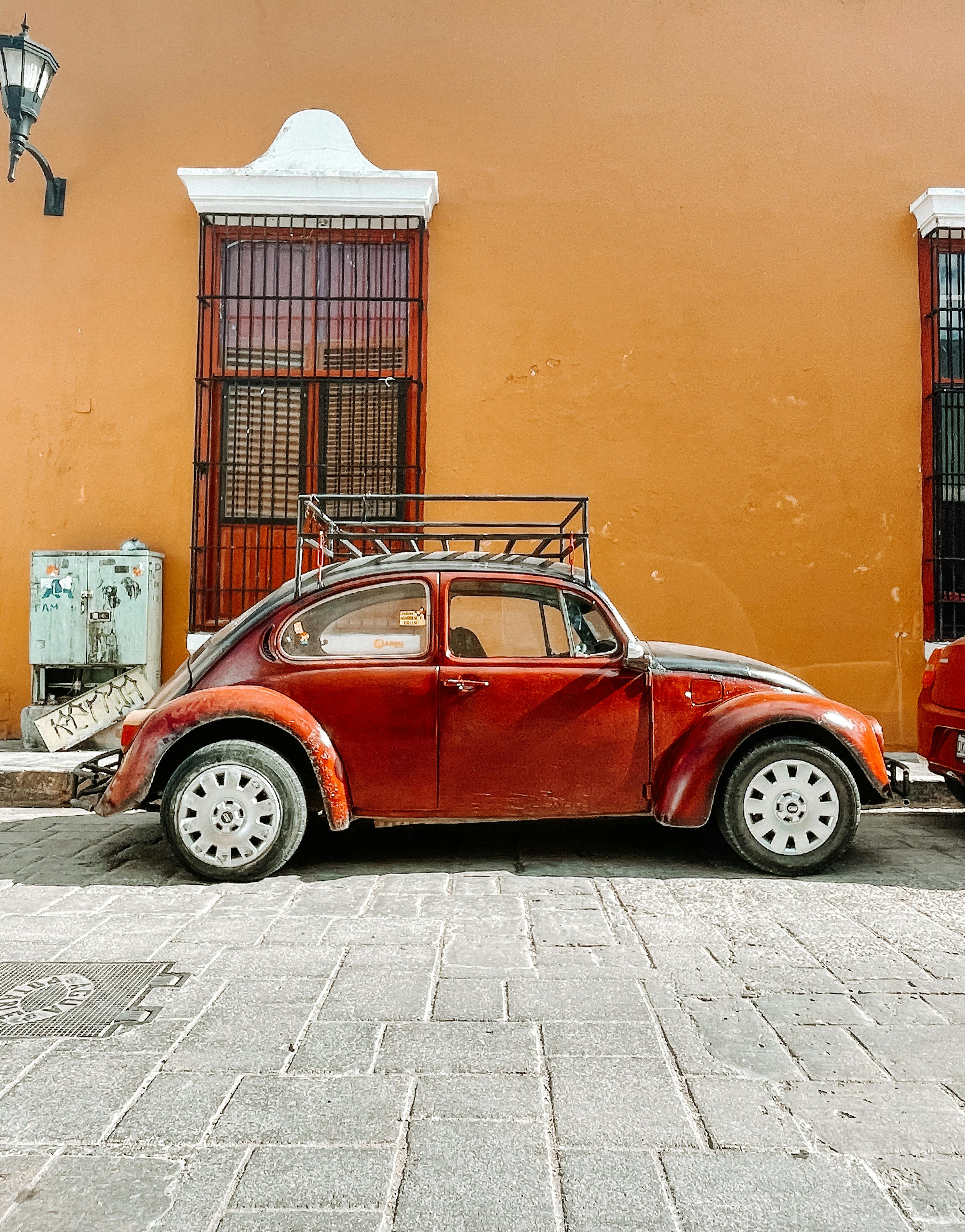 A classic red vintage car parked against a vibrant orange wall on a historic cobblestone street.