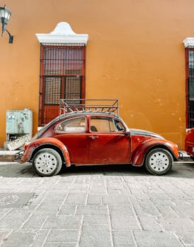 A classic red vintage car parked against a vibrant orange wall on a historic cobblestone street.
