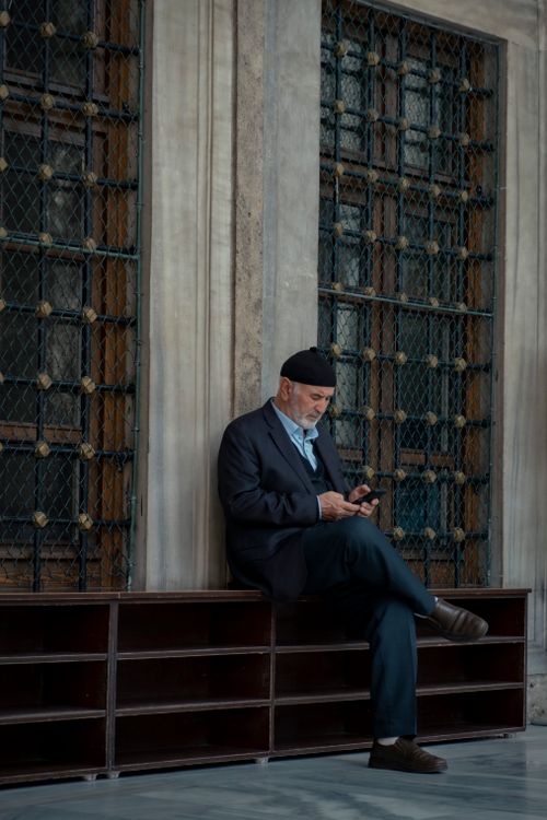 Free Elegant elderly man sitting with a smartphone in an urban environment, deep in thought. Stock Photo