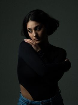 A woman posing thoughtfully in a dark studio, showcasing moody fashion photography.