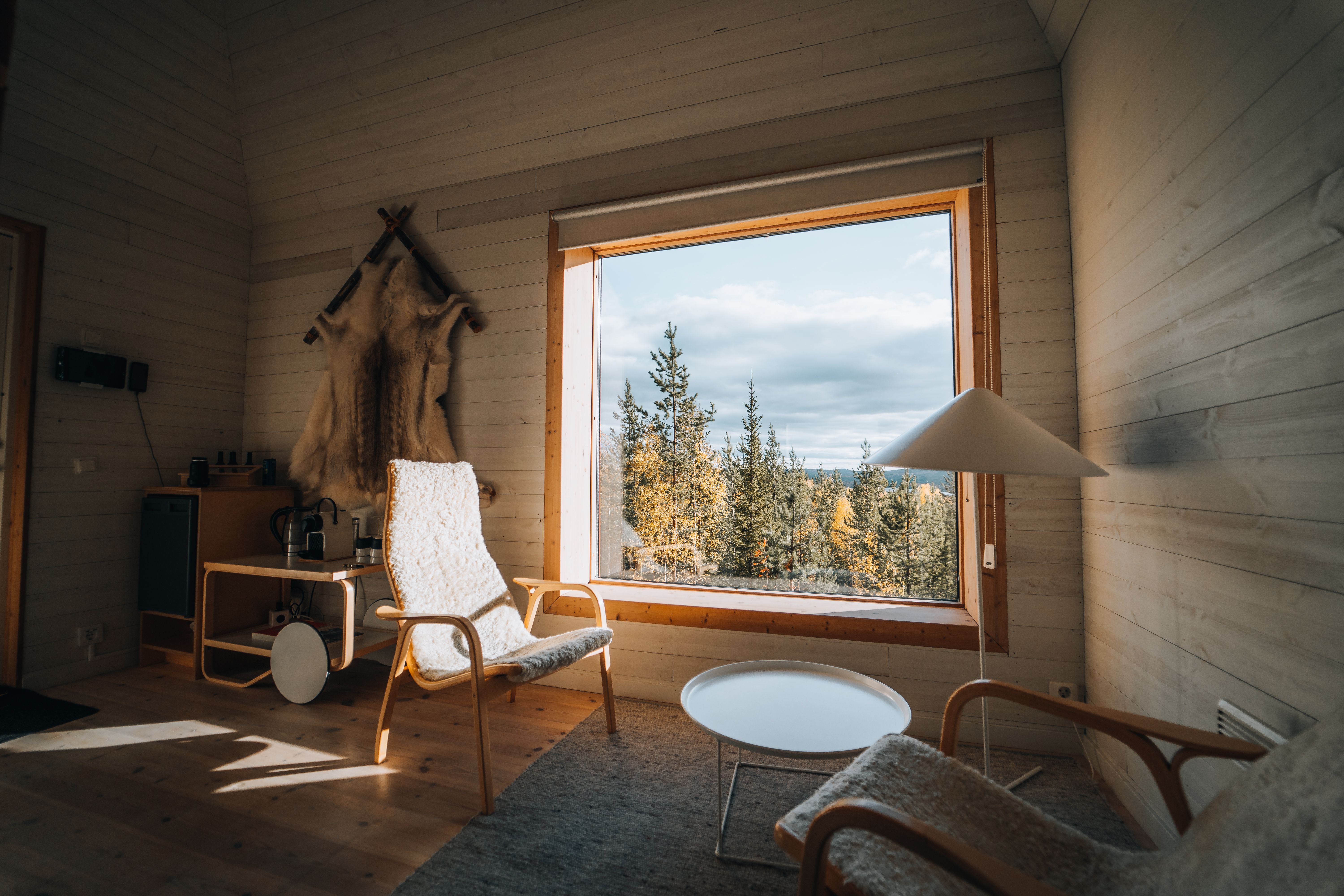 Warm cabin interior featuring natural wood decor and a large window overlooking a serene forest landscape.