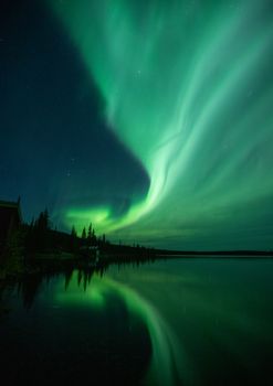 Mesmerizing aurora borealis reflecting on a serene lake under a starry night sky.