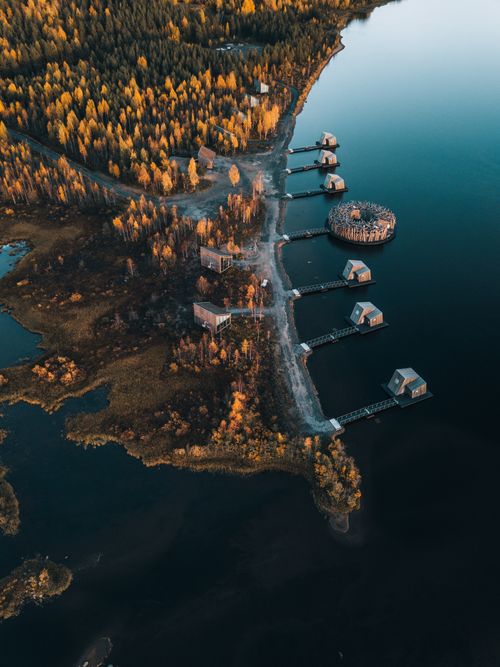 Free Aerial shot of charming floating cabins by a Swedish lakeside surrounded by autumn forest. Stock Photo