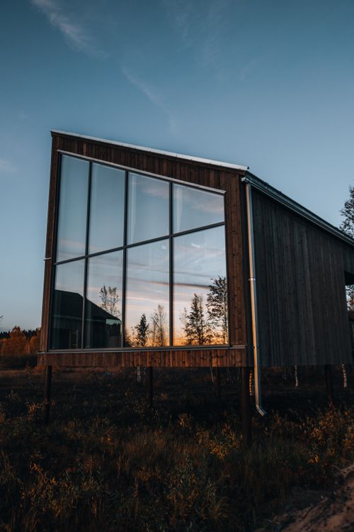Free A modern wooden building with large glass windows reflecting a vibrant sunset. Stock Photo