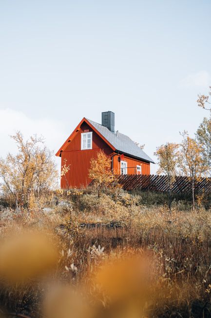 A charming red house surrounded by autumn foliage against a clear sky.