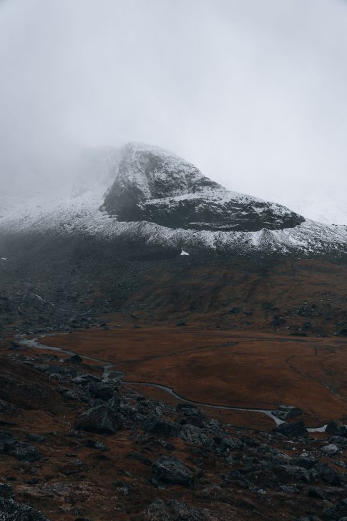 Free Dramatic mountain landscape with snow, rocks, and overcast skies creating a mysterious atmosphere. Stock Photo