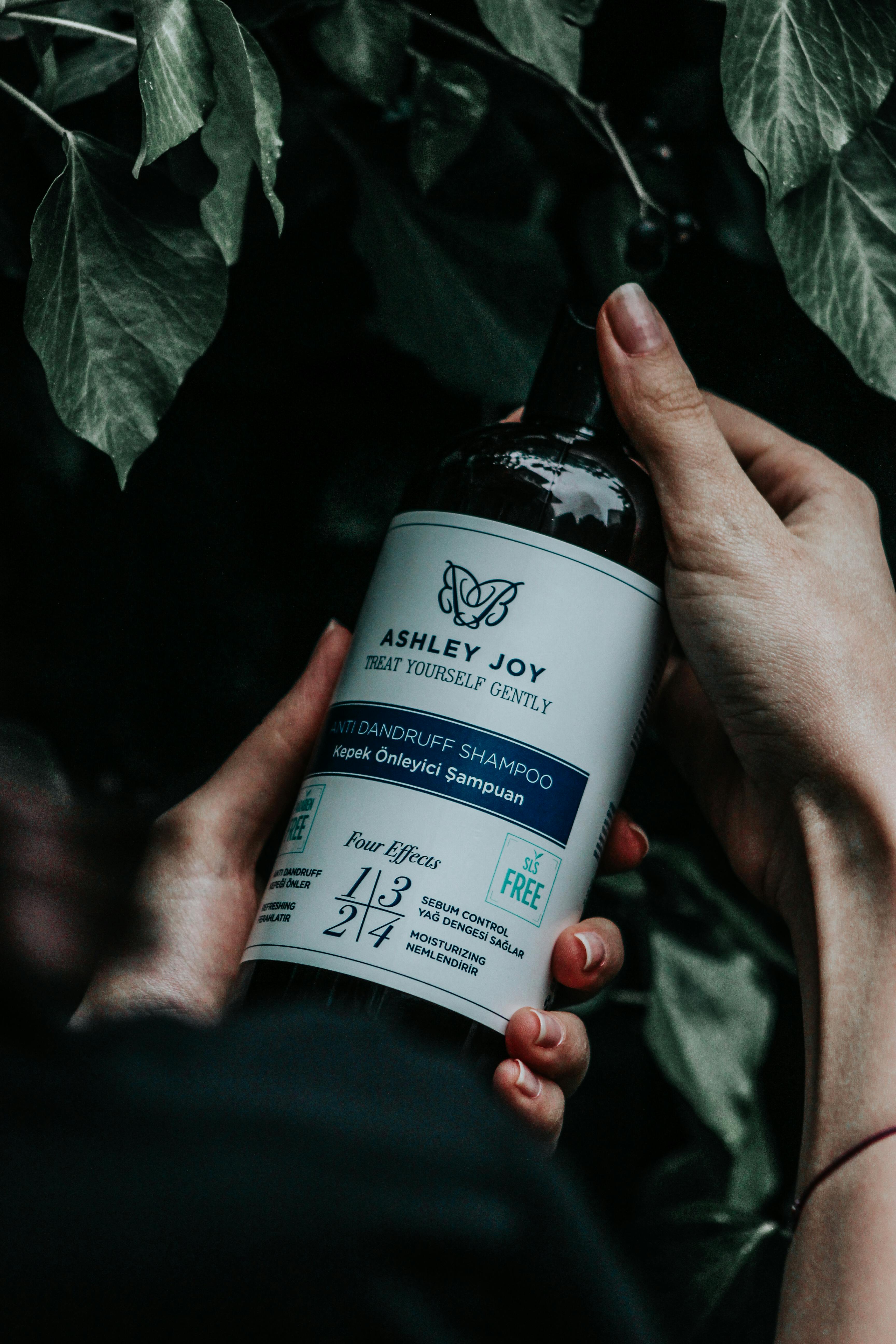 Hands holding a shampoo bottle against a leafy background, emphasizing natural hair care.
