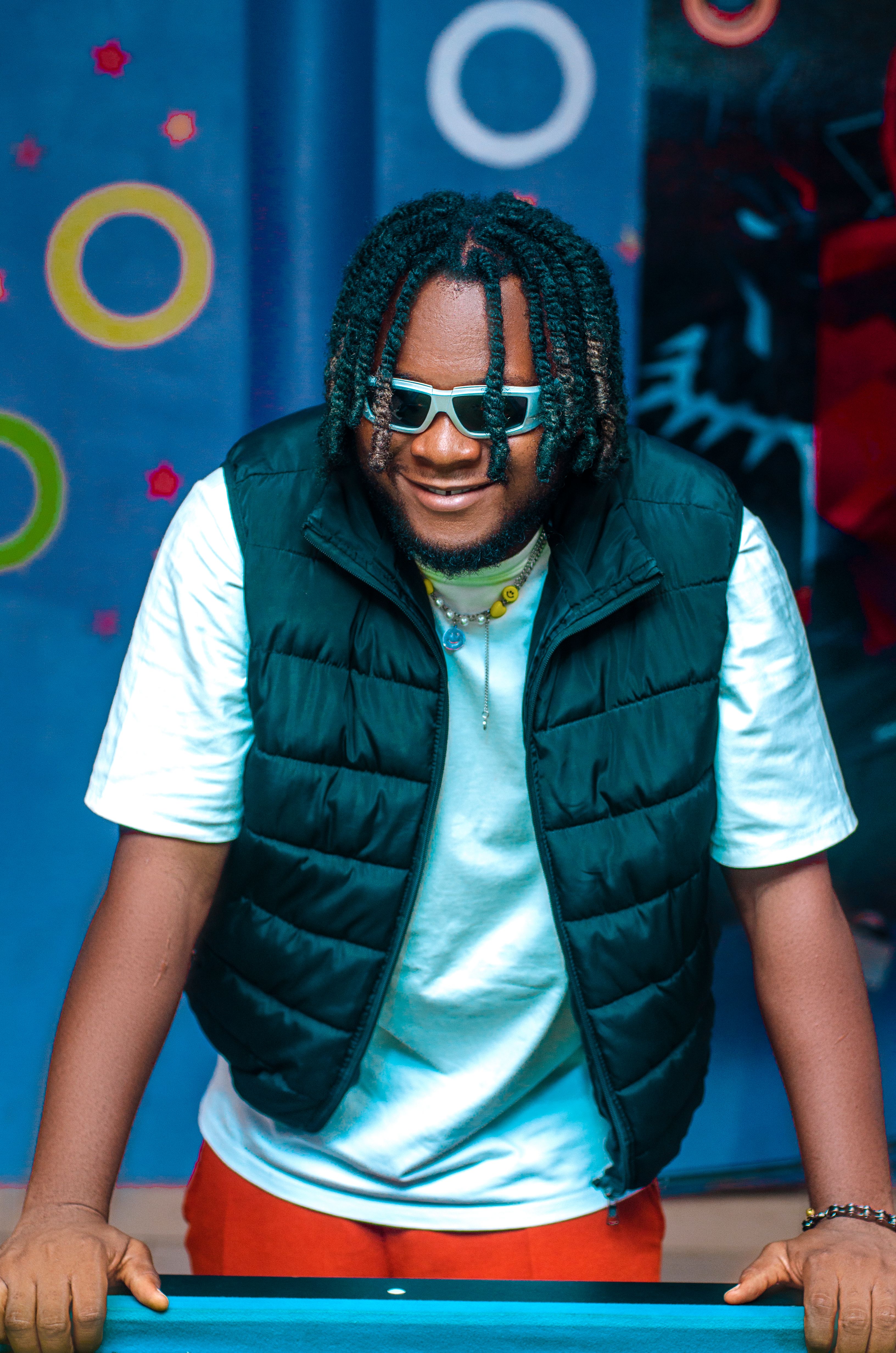 Fashionable man with dreadlocks and sunglasses posing indoors, exuding modern style and confidence.