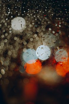 Captivating bokeh effect through a wet window, creating abstract light circles.