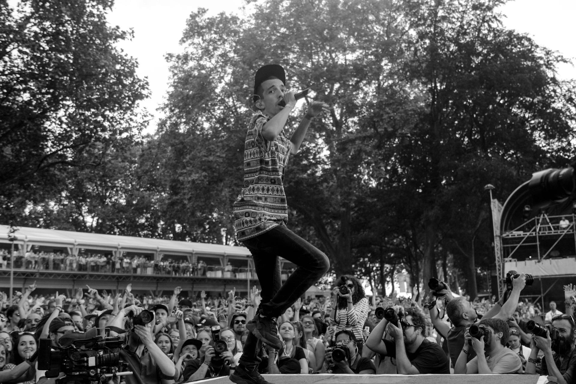 Energetic musician on stage with an enthusiastic crowd and media photographers.