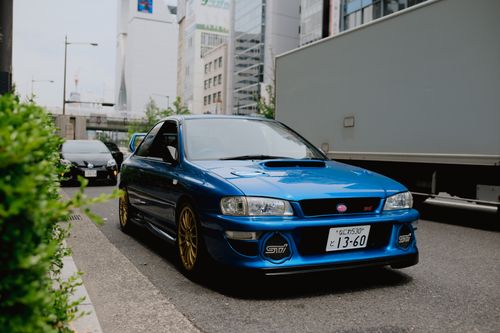 Free A blue sports car parked on a city street with modern buildings in the background, capturing urban life. Stock Photo