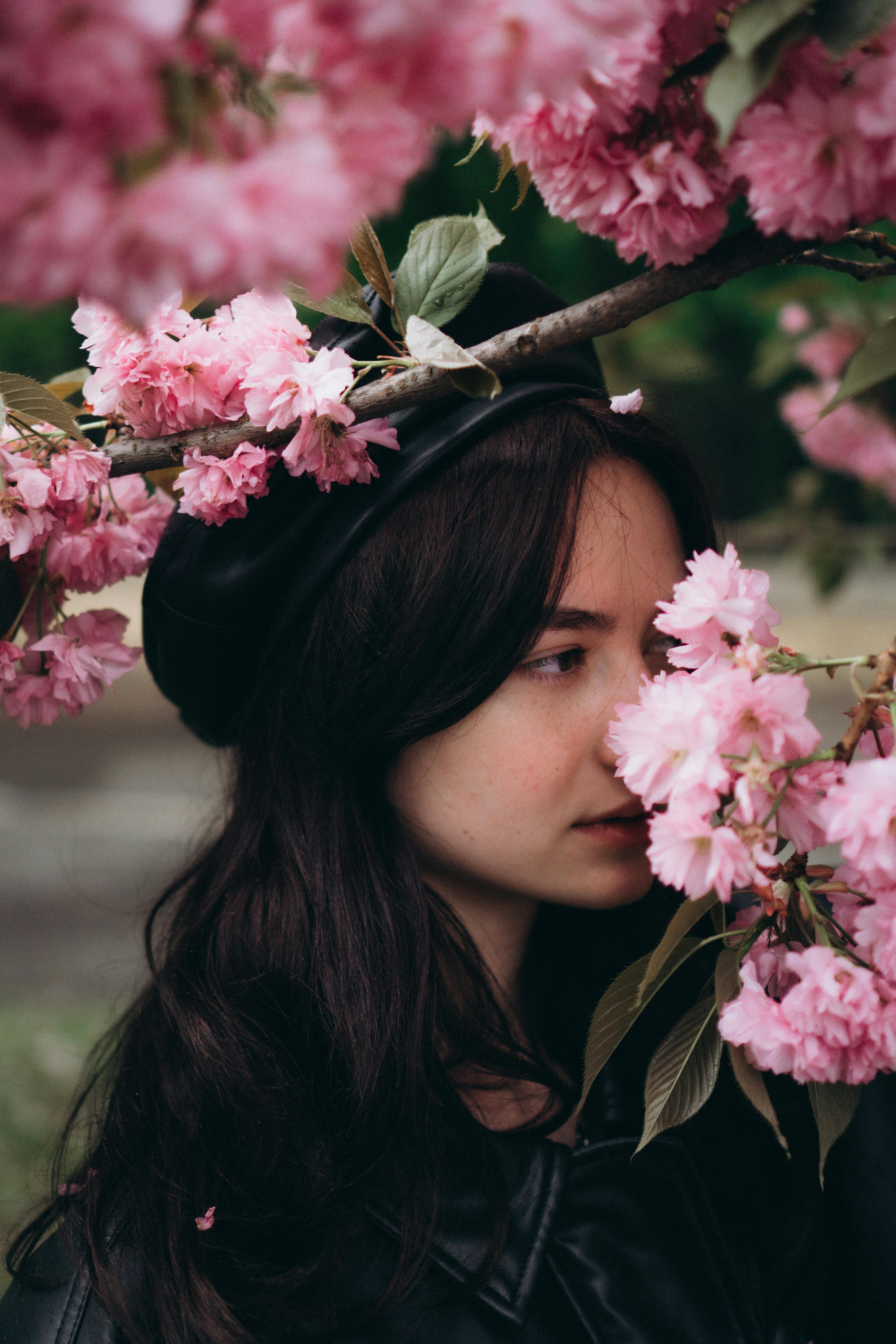 A woman with long dark hair surrounded by vibrant pink cherry blossoms in spring.