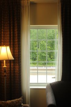 A cozy room interior with a lamp beside a window showcasing a lush greenery view.