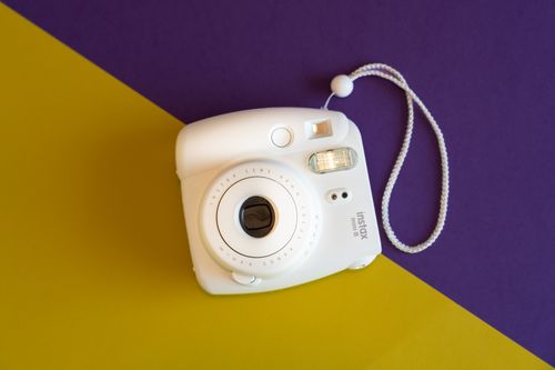 Free Top view of a white Instax Mini 8 camera on a vibrant purple and yellow background. Stock Photo