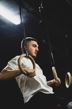 Focused adult male training on gymnastic rings in an indoor gym setting.