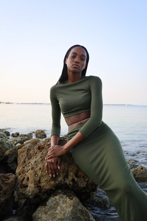 Woman in Green Clothes and Skirt Posing on Rocks on Sea Shore