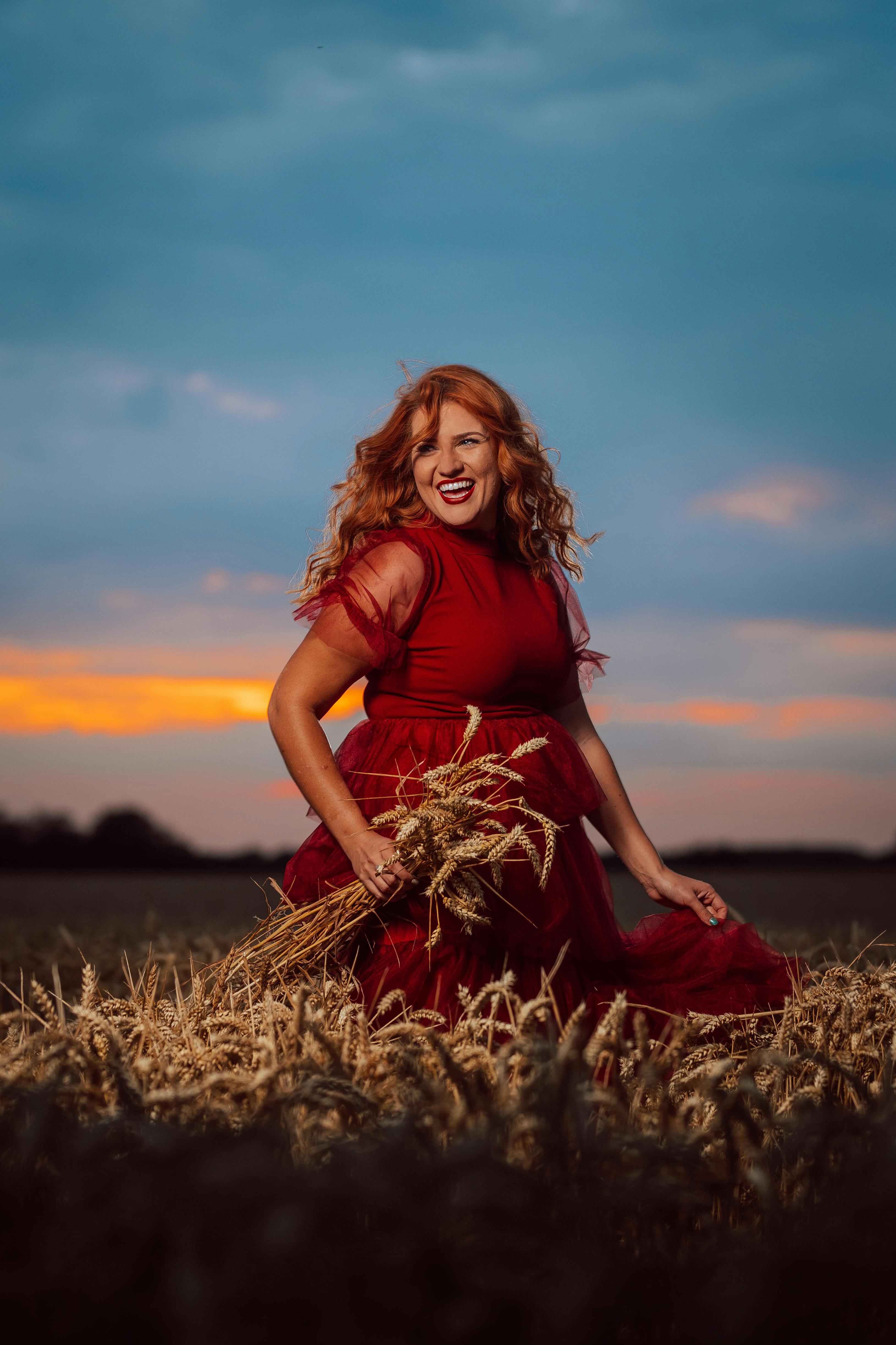 woman in a red dress standing in a field with a bunch of ears of grain