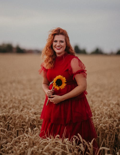 Smiling Woman in Red Dress and with Sunflower on Field