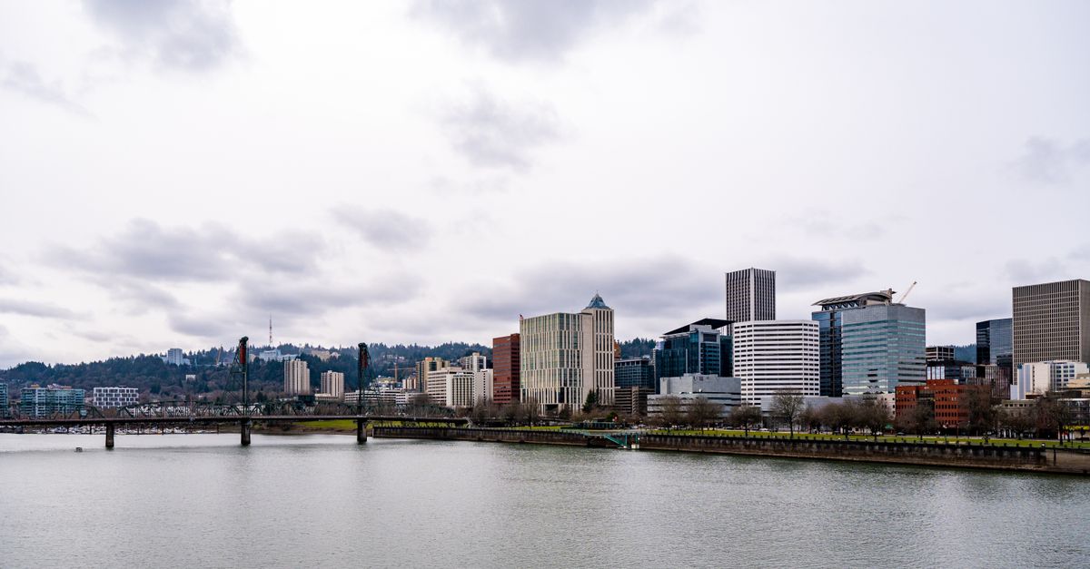 Portland cityscape featuring modern architecture under cloudy sky, viewed from the Willamette River.