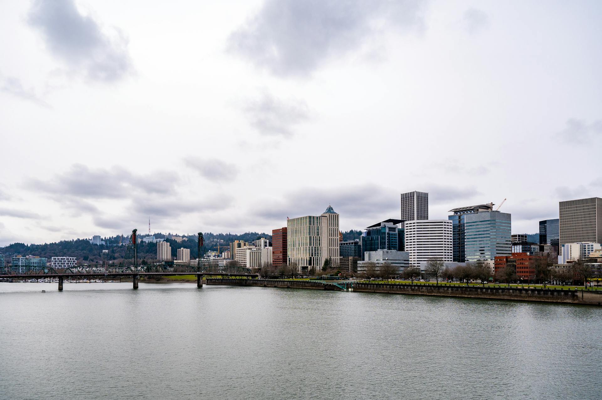 Portland cityscape featuring modern architecture under cloudy sky, viewed from the Willamette River.