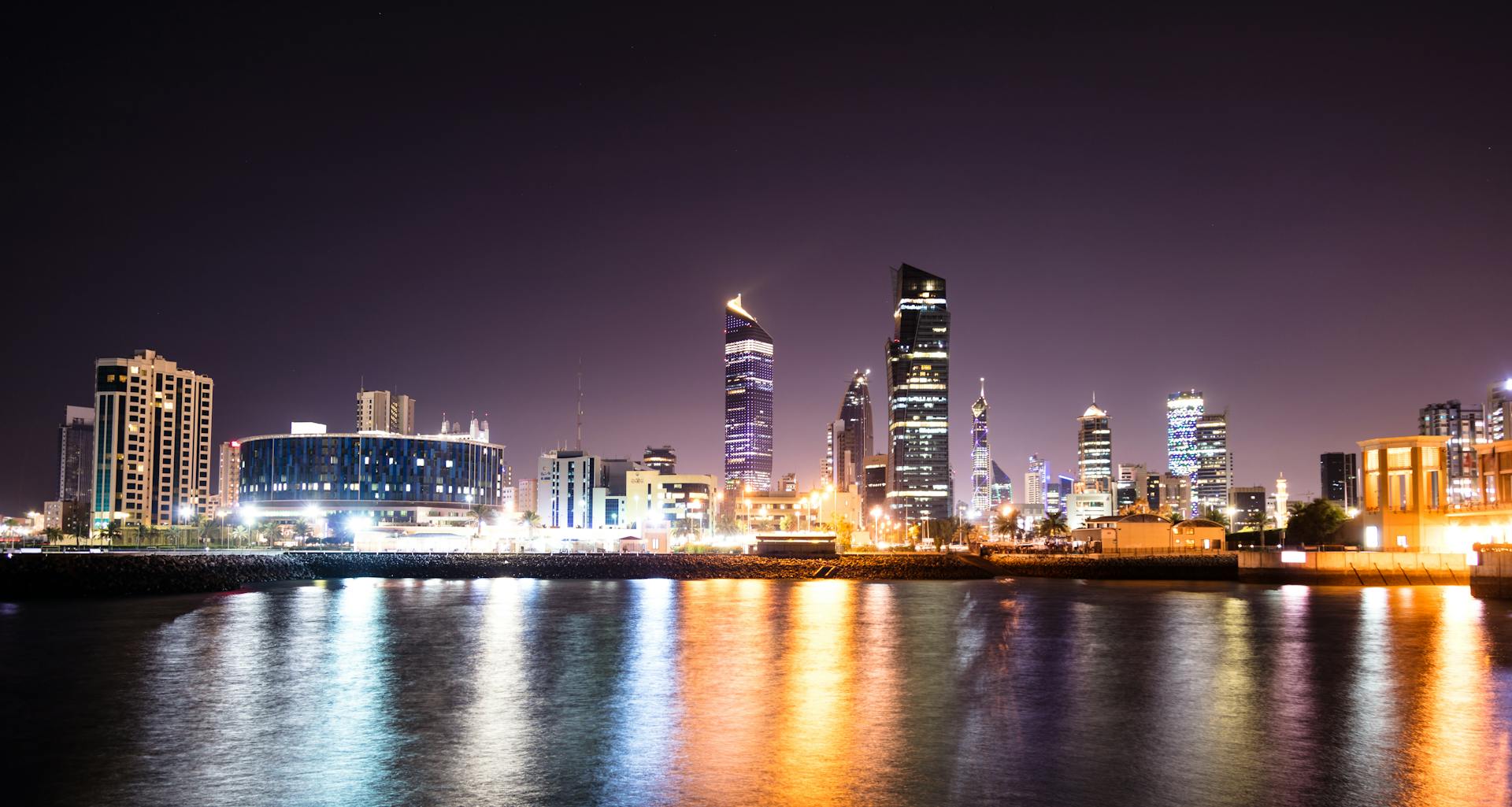 Kuwait City skyline with illuminated skyscrapers and reflections at night.