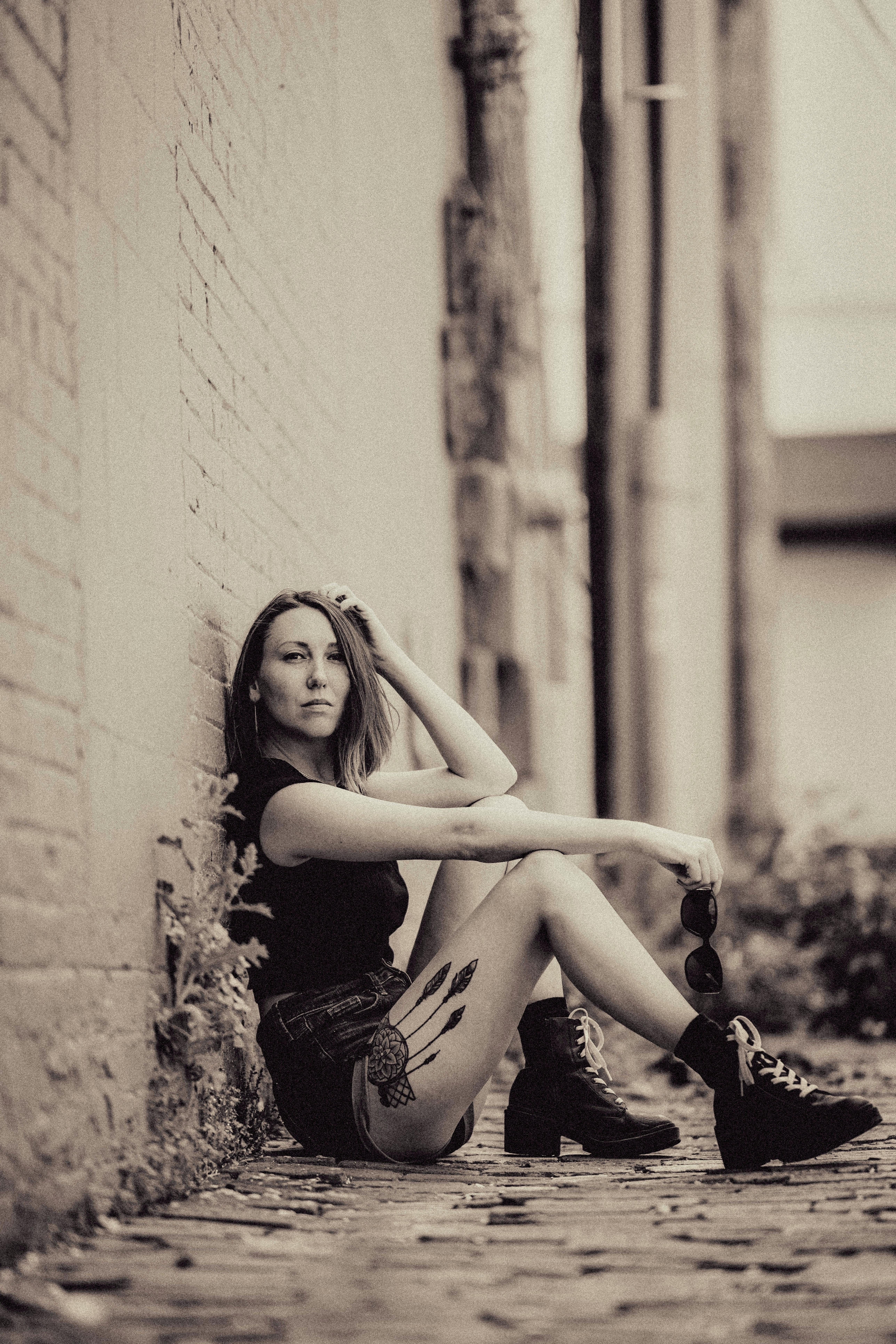 a woman sitting on the ground in front of a brick wall