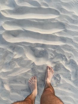 A man stands barefoot on rippled sand, capturing textures and tranquility.