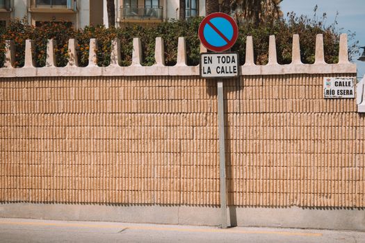 A street view in Málaga, Spain showing a no parking sign on a brick wall under clear skies.