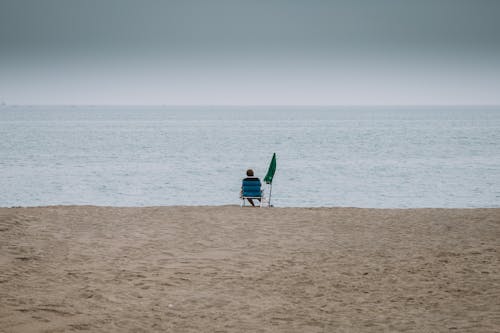 Person Sitting on Beach under Clouds