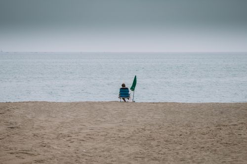 Free A solitary figure in a beach chair faces the calm sea on an overcast day in Málaga, Spain. Stock Photo