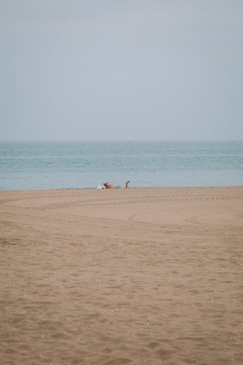 A Person Sunbathing on the Beach in Distance 