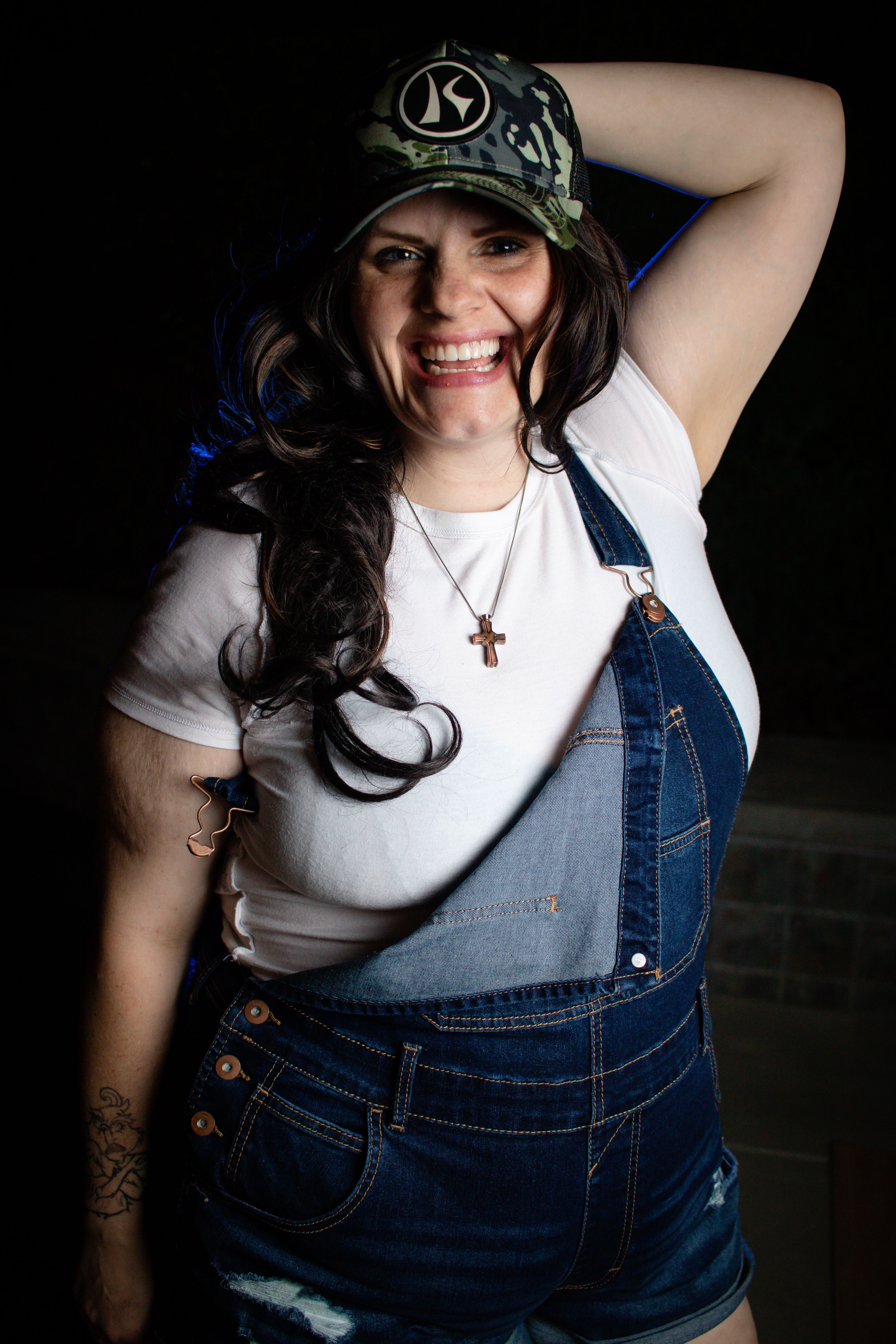 Portrait of a cheerful woman in denim overalls and a baseball cap, smiling confidently.