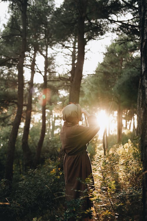 Woman Standing in the Forest with Sun Shining between the Trees 