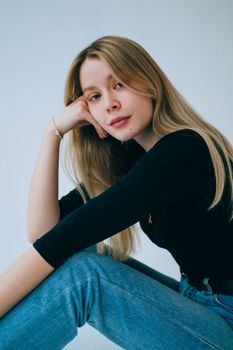 Stylish portrait of a young blonde woman in casual attire, sitting indoors.