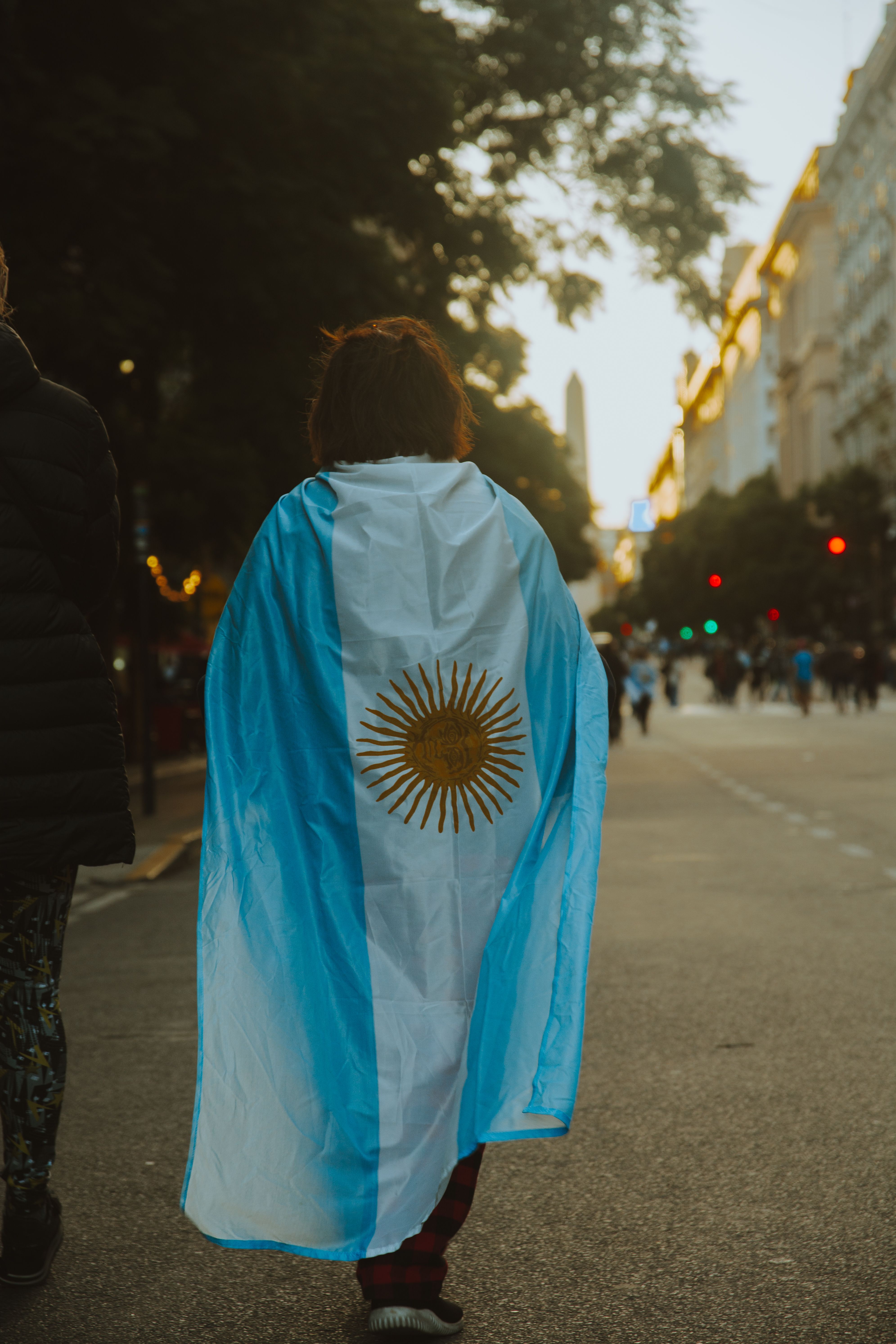 A person draped in the Argentine flag walking through city streets at twilight, conveying a sense of patriotism.