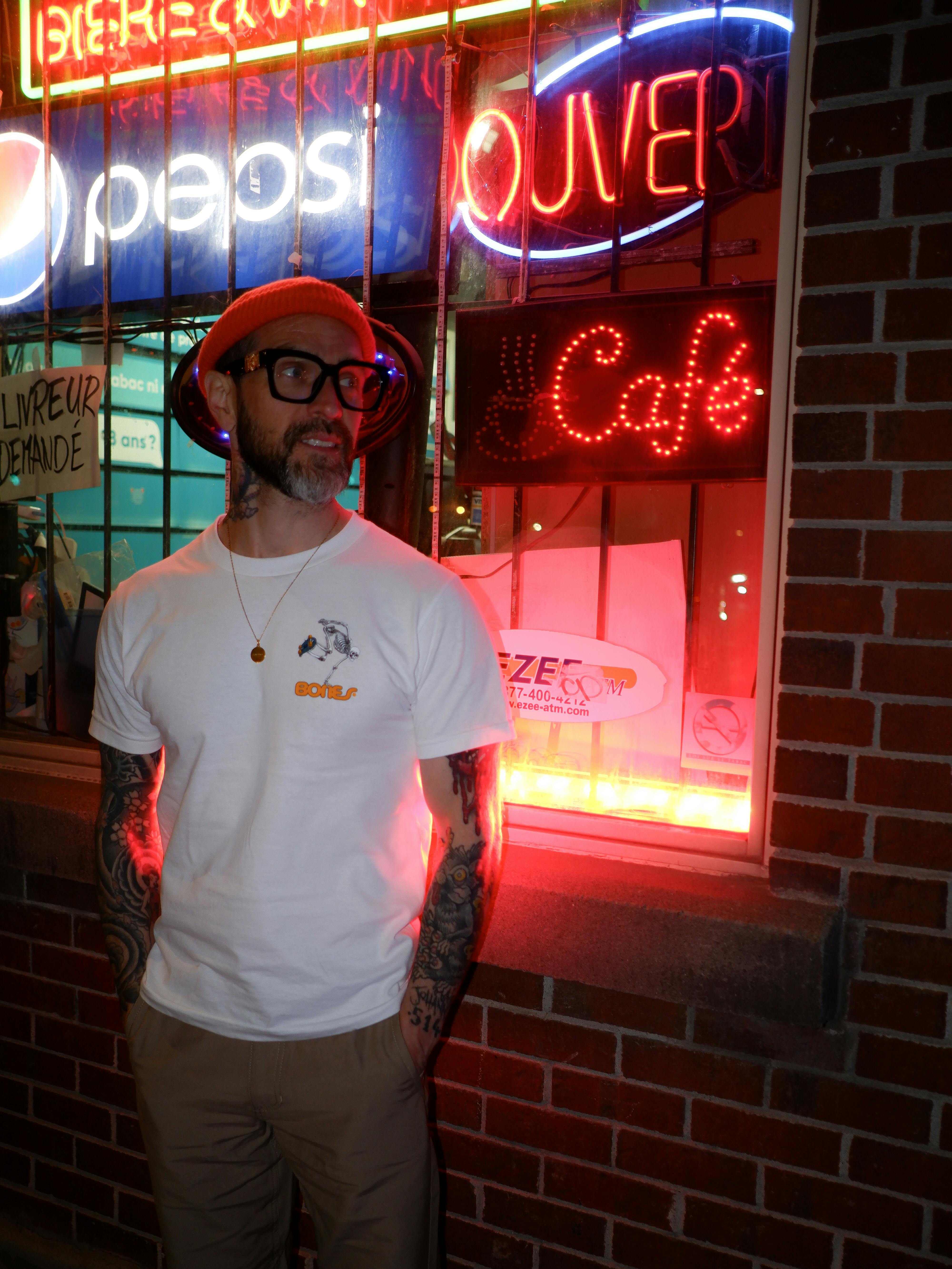 Portrait of a man beside neon signs on a Montreal street at night, showcasing urban fashion.